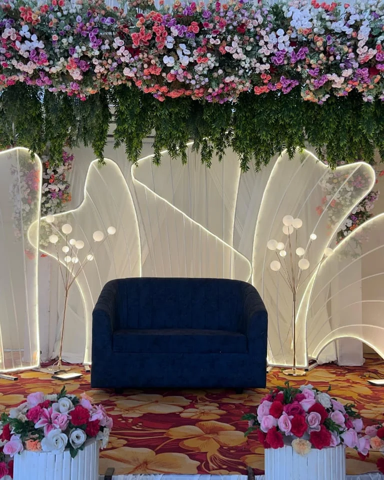 Stage under a canopy of flowers with glowing white panels and a blue sofa