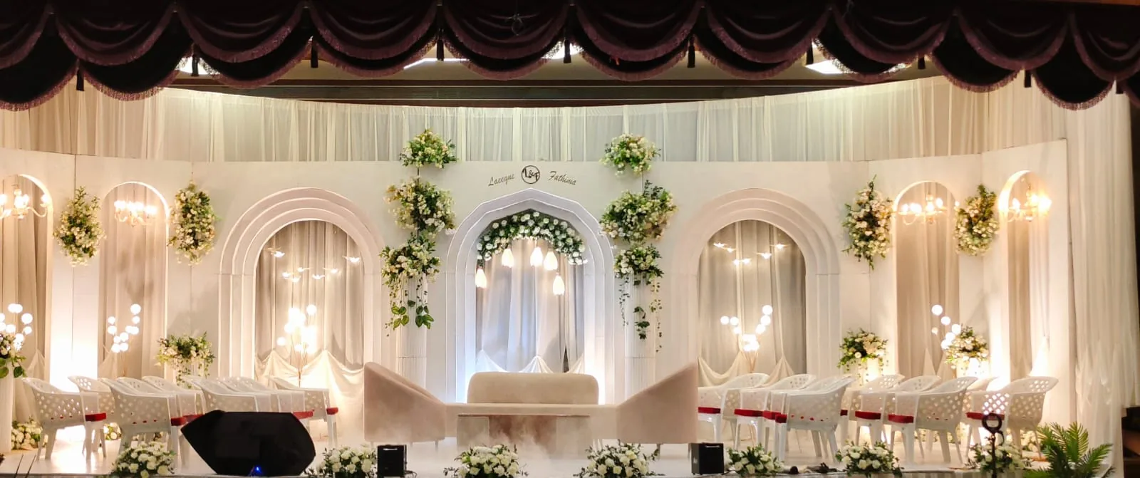 White arched wedding stage with greenery and chandeliers
