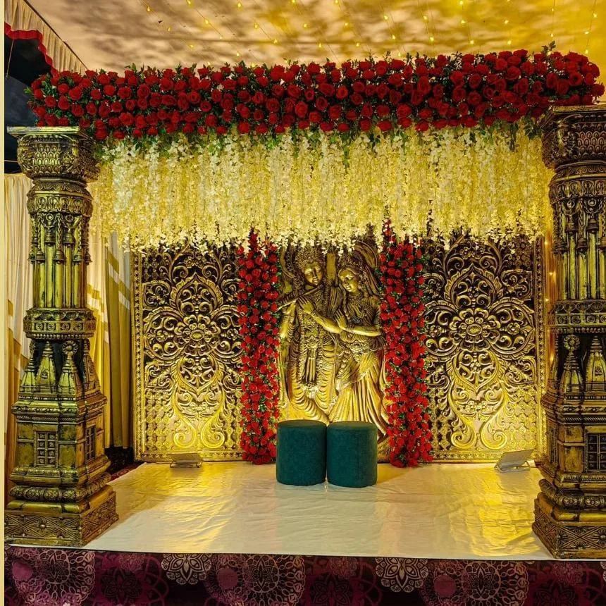 Golden carved stage with a Radha-Krishna backdrop and red roses